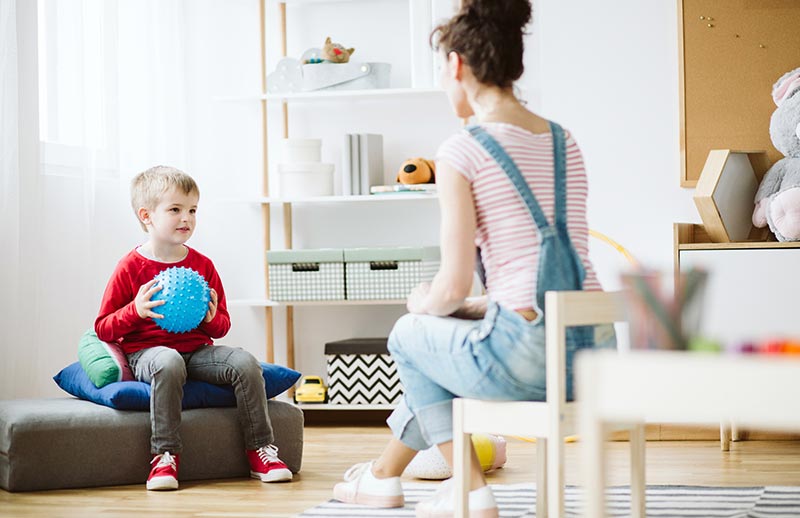 woman in overalls talking to a boy holding a blue ball